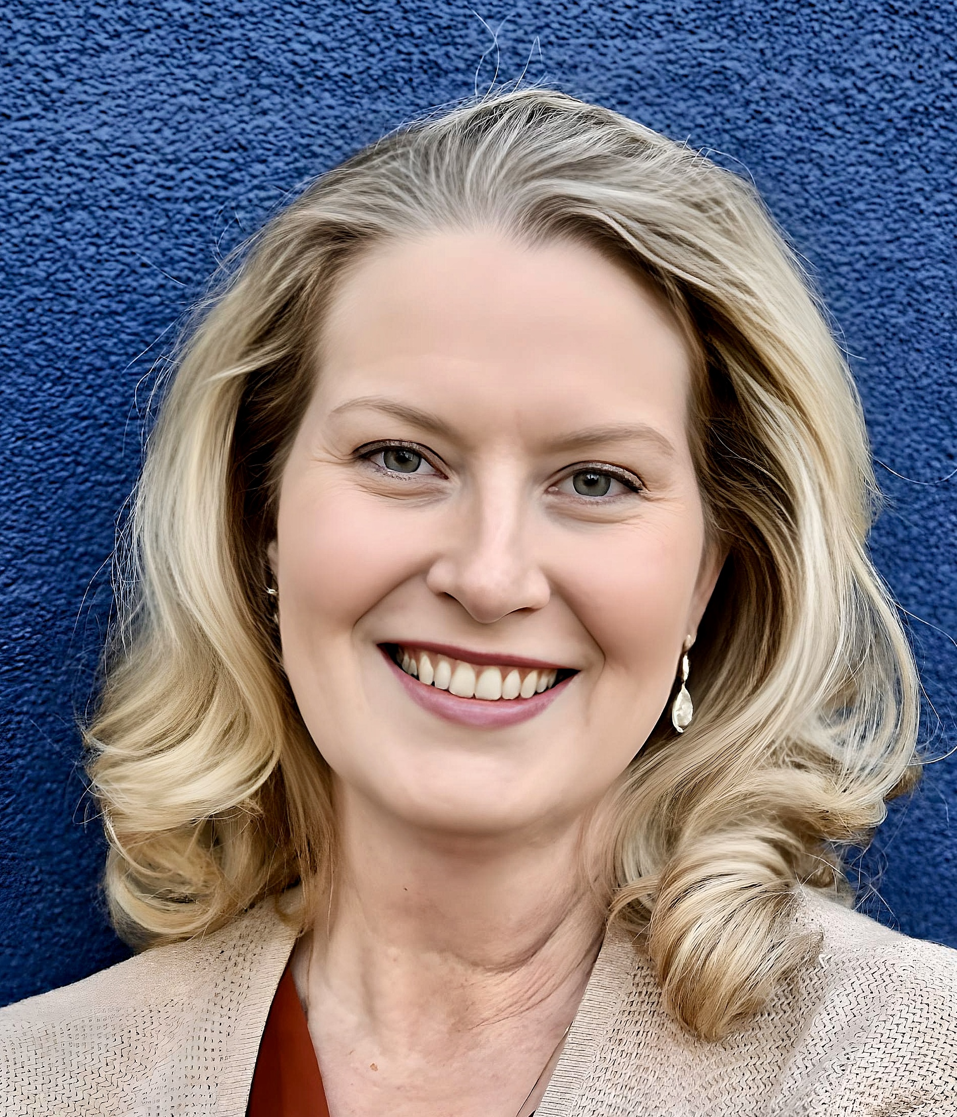 Picture of Celeste Sodergren, a woman with blonde hair standing against a blue background, smiling.